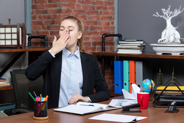 Top view of young female sitting at a table and yawning in the office