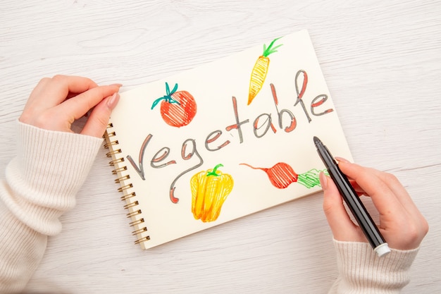 Top view young female writing and drawing on notepad on white desk