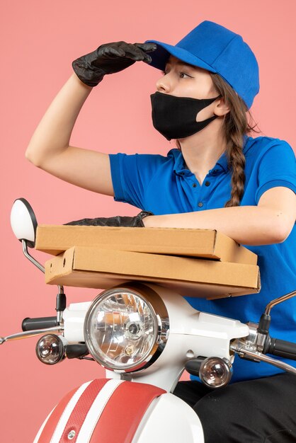 Top view of young focused female courier wearing medical mask and gloves holding boxes on pastel peach