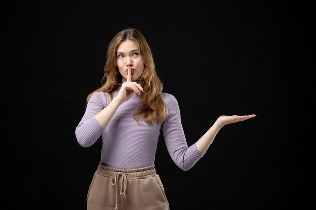 Top view of young girl pointing something and making silence gesture on dark
