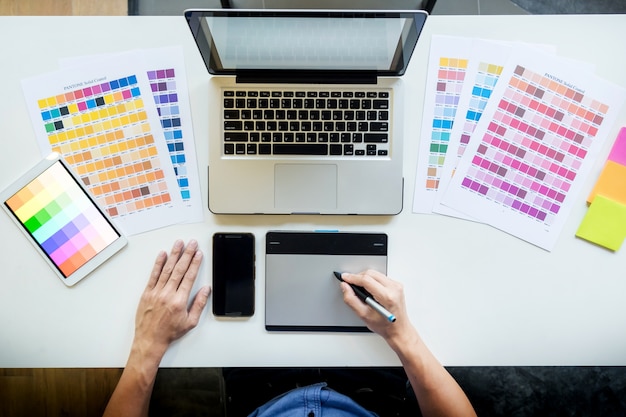 Top view of a young graphic designer working on a desktop computer and using some color swatches, top view.