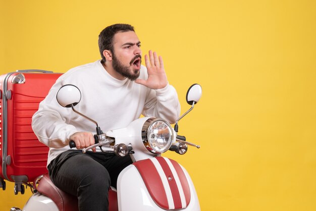 Вид сверху на молодого парня, сидящего на мотоцикле с чемоданом и вызывающего кого-то с удивленным выражением лица на изолированном желтом фоне