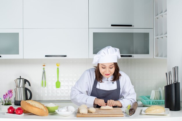 Top view of young happy female chef in uniform standing behind table preparing pastry in the white kitchen