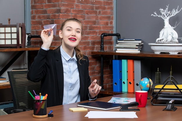 Free photo top view of young happy smiling female office worker sitting at her desk and playing paper plane