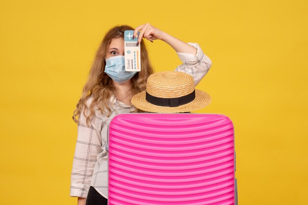 Top view of young lady wearing mask showing ticket and standing behind her pink bag