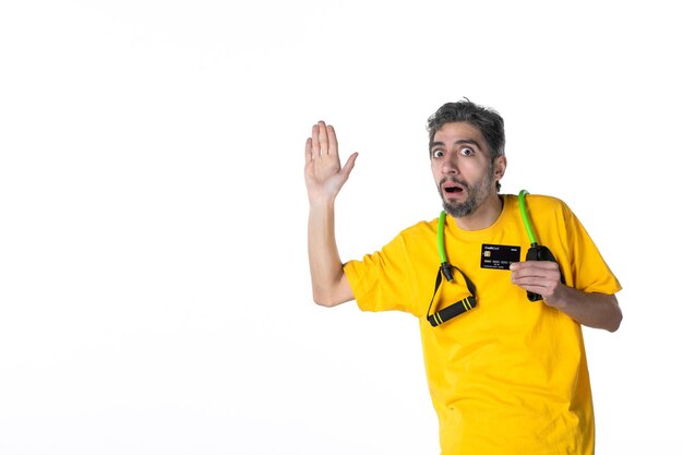 Top view of young male in yellow shirt and holding sport accessory with rope and showing bank card feeling angry on white surface