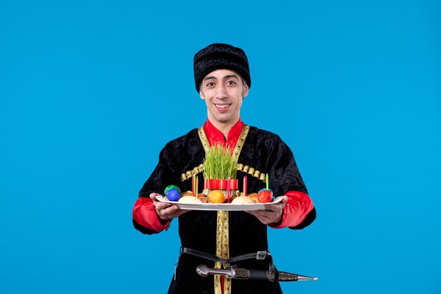 Top view of young man in traditional dress holding tray filled with national confectionery on blue background