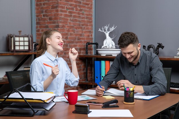 Вид сверху молодых целеустремленных и трудолюбивых улыбающихся офисных работников, сосредоточенных на одной проблеме в офисной среде