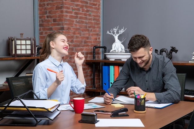 Вид сверху молодых целеустремленных и трудолюбивых улыбающихся офисных работников, сосредоточенных на одной проблеме в офисной среде