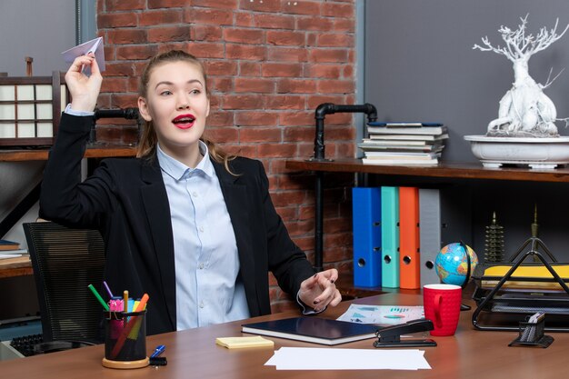 Top view of young positive female office worker sitting at her desk and playing paper plane