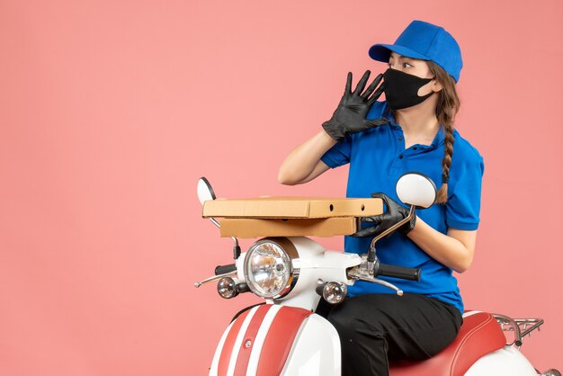 Top view of young scared female courier wearing medical mask and gloves sitting on scooter delivering orders on pastel peach