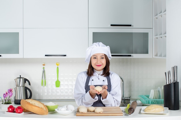 白いキッチンでペストリーを準備するテーブルの後ろに立っている制服を着た若い笑顔の女性シェフの上面図