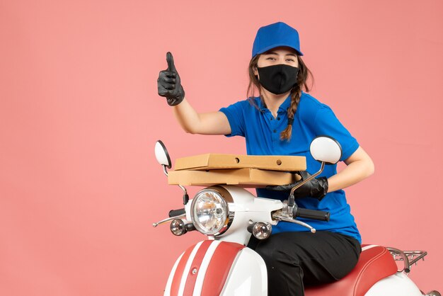 Top view of young smiling female courier wearing medical mask and gloves sitting on scooter