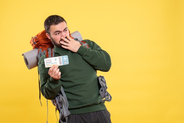 Top view of young surprised travelling guy with backpack and showing ticket feeling confused on yellow