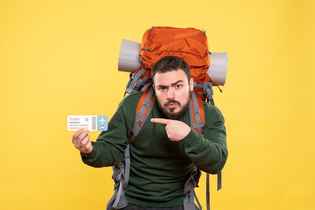 Free photo top view of young travelling guy with backpack and showing ticket feeling confused on yellow