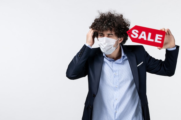 Top view of young unsure uncertain business person in suit and wearing his mask showing sale inscription posing for camera