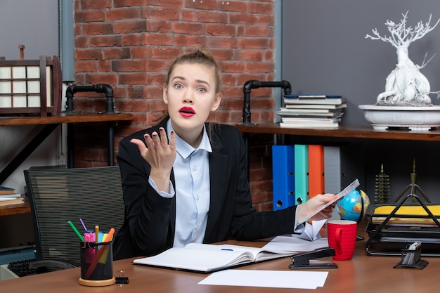 Free photo top view of young woman sitting at a table and holding a document worried for something in the office