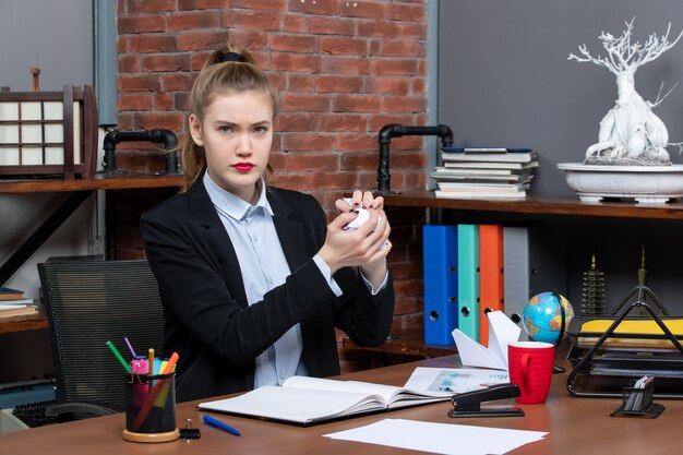 Top view of young woman sitting at a table and holding wrapped paper in the office