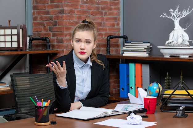 Top view of young woman sitting at a table and questioning someone in the office