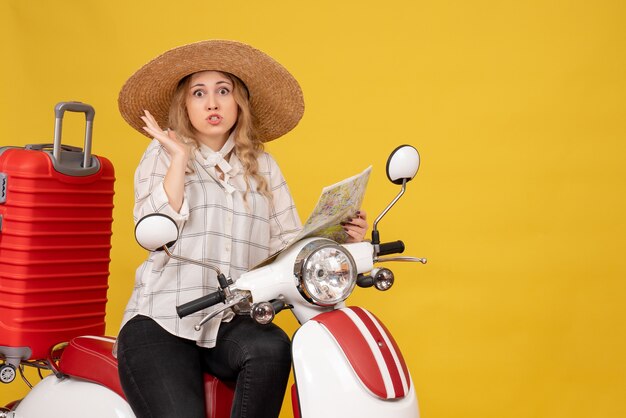 Top view of young woman wearing hat and sitting on motorcycle and holding map feeling confused on yellow 