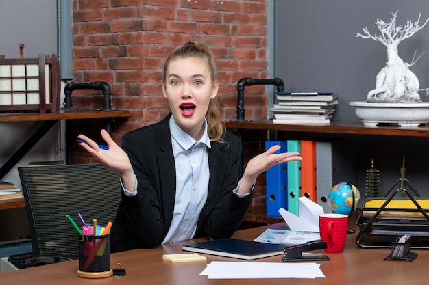 Top view of young wondered and emotional female assistant sitting at her desk in the office