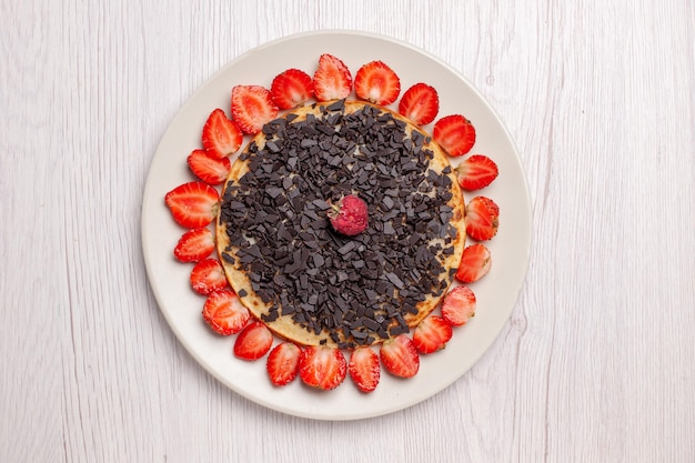 Top view of yummy baked pancakes with strawberries and chocolate chips on white table