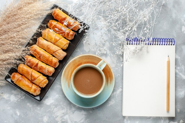Вид сверху вкусные браслеты с молочным кофе и блокнотом на сером столе кондитерский торт бисквитный сладкий сахар