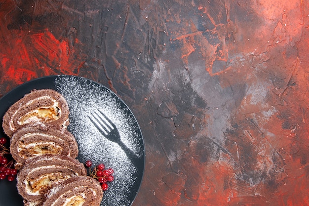 Вид сверху вкусные бисквитные рулеты внутри тарелки на темном фоне
