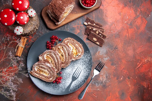 Вид сверху вкусных бисквитных рулетов внутри тарелки на темном столе