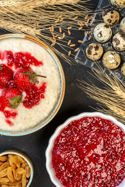 Free photo top view of yummy breakfast served with strawberries jam in a bowl and yellow raisins spikes eggs on dark color background