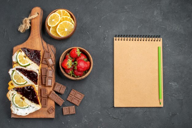 Top view yummy cake slices with chocolate and fruits on dark surface