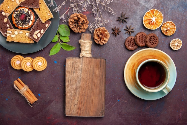 Top view of yummy cake slices with cookies and cup of tea on black