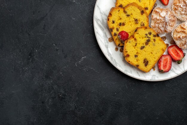 Vista dall'alto deliziose fette di torta con fragole rosse fresche e biscotti sulla scrivania grigia