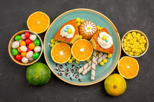 Top view yummy cake slices with fresh sliced tangerines and candies on a dark