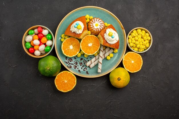 Top view yummy cake slices with fresh sliced tangerines and candies on dark