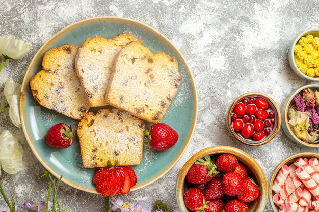 Вид сверху вкусные кусочки торта с фруктами и конфетами на свете