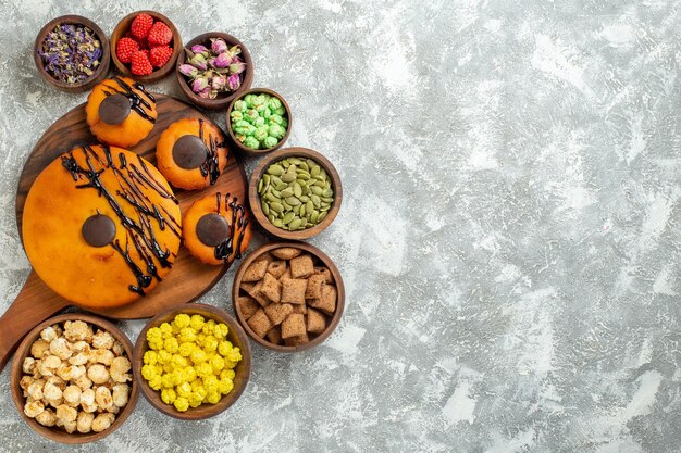 Top view yummy cakes with chocolate icing and candies on a white surface cake cocoa biscuit pie dessert sweet cookie