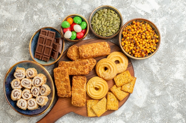 Top view yummy cakes with cookies and candies on light white background