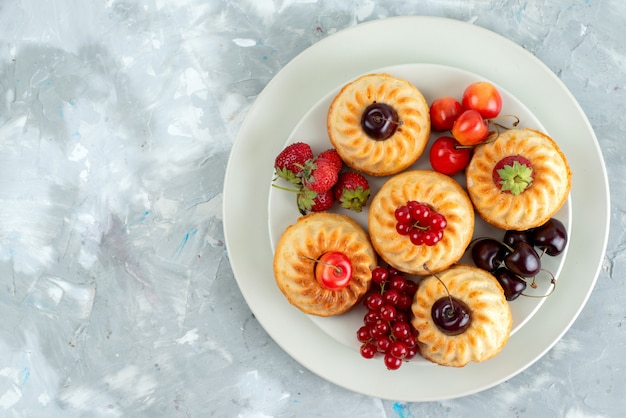 A top view yummy cakes with mellow and juicy red fruits inside white plate berry fruit cake 