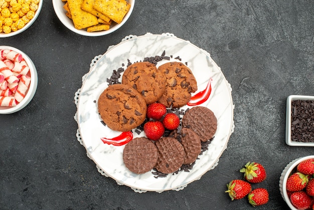 Вкусное шоколадное печенье с разными закусками на темном полу, сладкое печенье, вид сверху