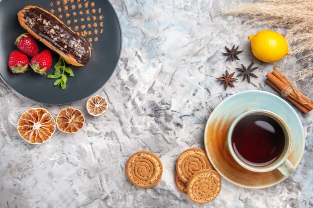 Top view yummy choco eclairs with cup of tea on light biscuit cookie dessert