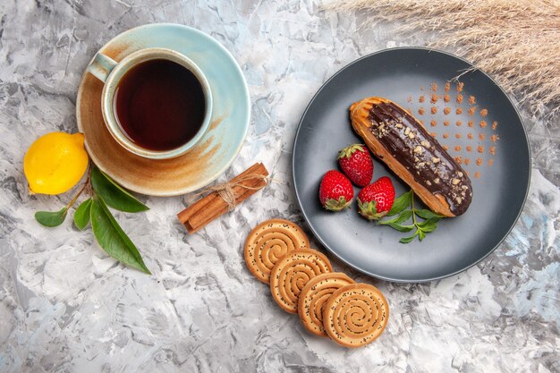 Top view yummy choco eclairs with cup of tea on light biscuit cookies dessert