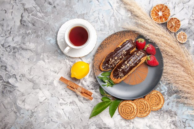 Top view yummy choco eclairs with cup of tea on light white cake dessert biscuit