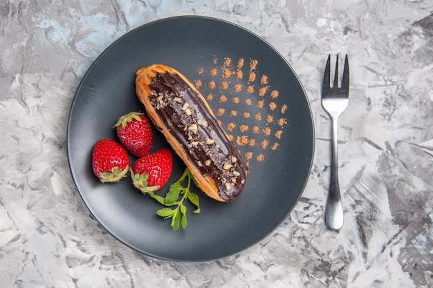Top view yummy choco eclairs with strawberries on light cake dessert candy
