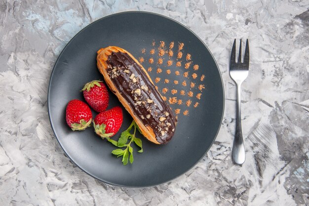 Top view yummy choco eclairs with strawberries on light cake dessert candy