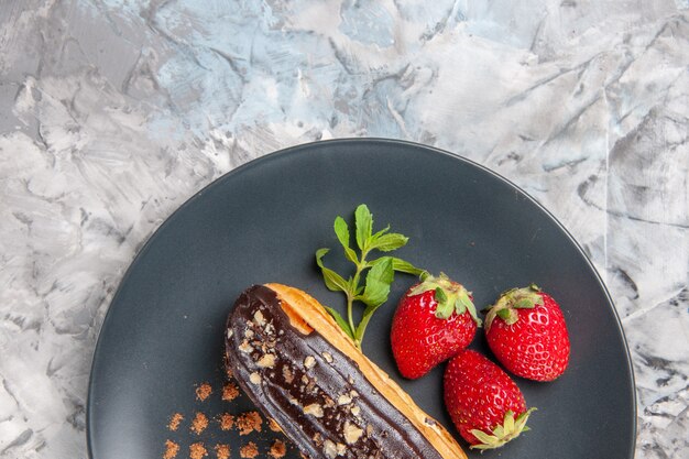 Top view yummy choco eclairs with strawberries on light dessert cake candy