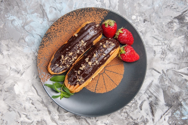 Бесплатное фото Вкусные шоколадные эклеры с клубникой на легком десертном бисквитном печенье, вид сверху