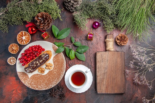 Вид сверху вкусные шоколадные эклеры с чаем и ягодами на темном столе, пирог, сладкий торт, десерт