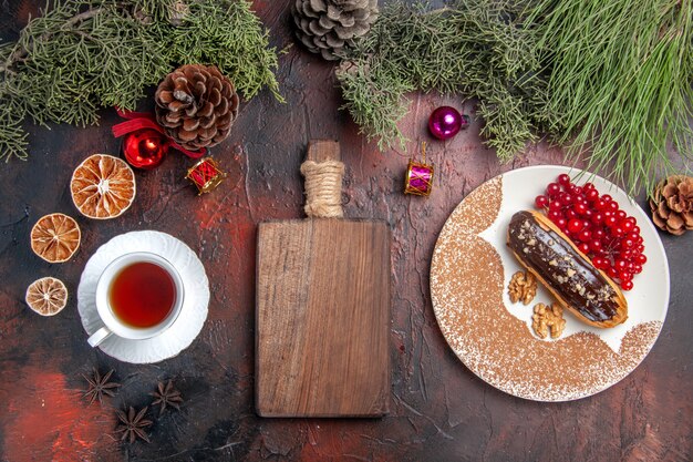 Вид сверху вкусные шоколадные эклеры с чаем и ягодами на темном столовом пироге, сладком десертном пироге