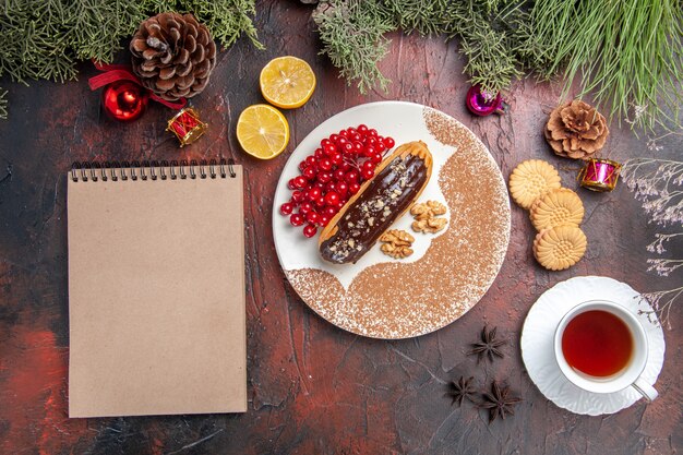 Вид сверху вкусные шоколадные эклеры с чаем и ягодами на темном столе, сладкий торт, пирог, десерт
